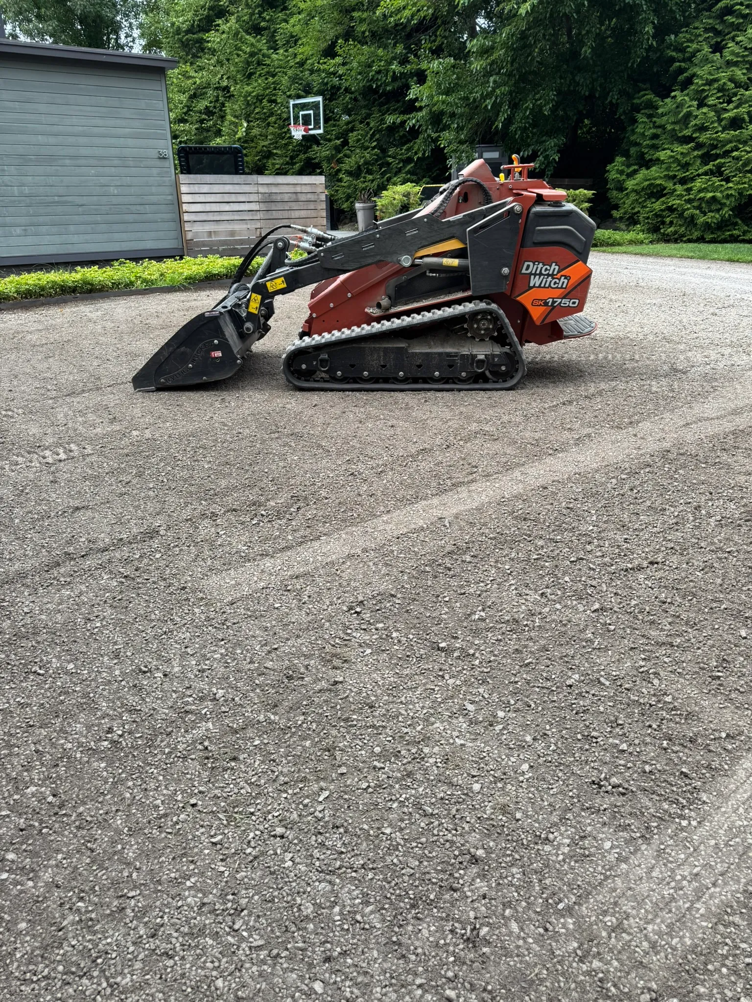 A Tringale Landscaping mini skid steer working a narrow gravel drive with tight access